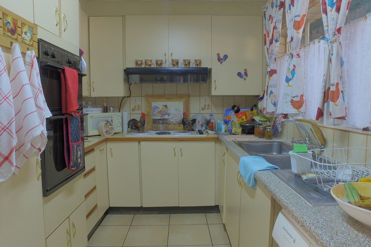 A compact kitchen featuring built-in cabinetry, a double wall oven, an extractor fan, and a stainless steel sink with tiled splashbacks.