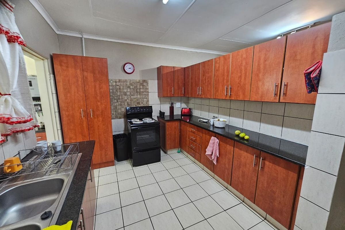 A functional kitchen featuring wood-look cabinetry, dark granite countertops, tiled flooring, and a built-in stove with an integrated workspace.