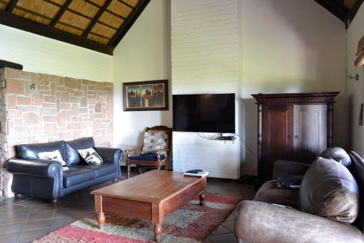 Spacious living room featuring a high vaulted thatched ceiling, exposed stone feature wall, and a prominent white brick fireplace.