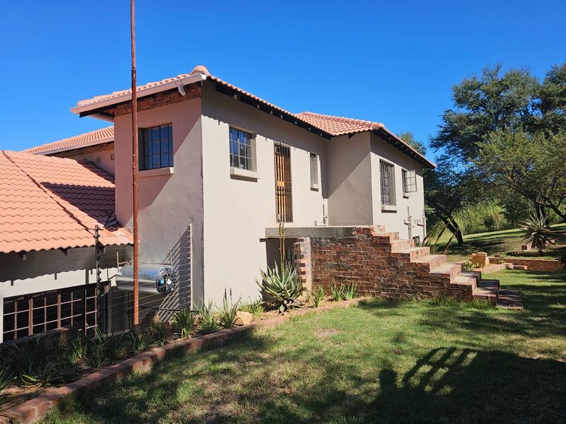 Rear exterior view of the farm property featuring a tiled roof, brick staircase, and established garden surroundings.