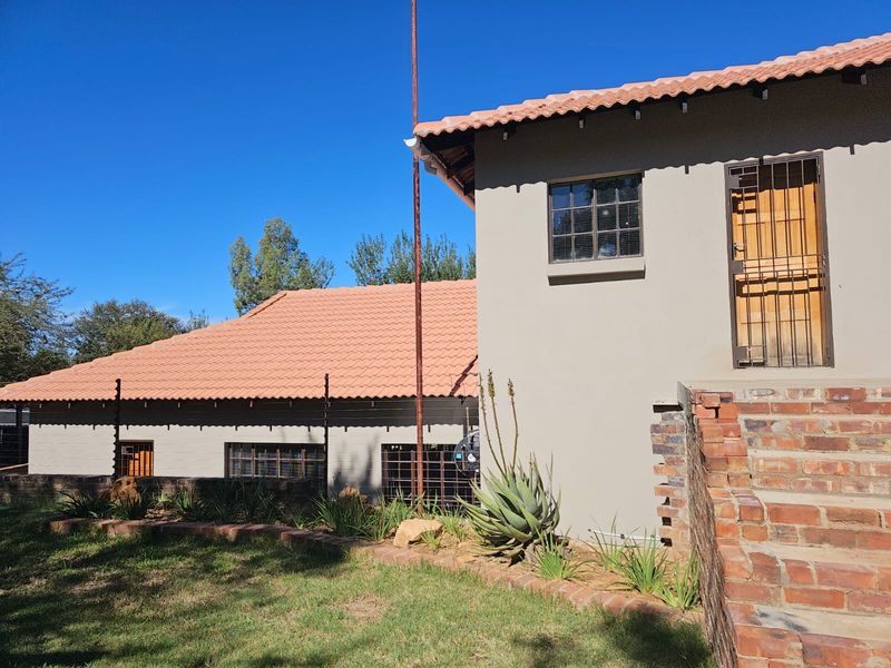 Rear view of the farm property featuring terracotta tiled roofing, brick staircase, and established garden beds with security fencing.