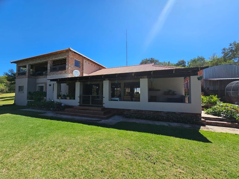 A spacious rear exterior view of the farmhouse featuring a covered patio, brick masonry, and a large, well-maintained lawn area.