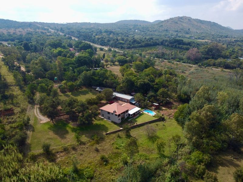 Aerial view of a farm property featuring a main residence, swimming pool, and surrounding landscaped grounds set within a scenic rural landscape.