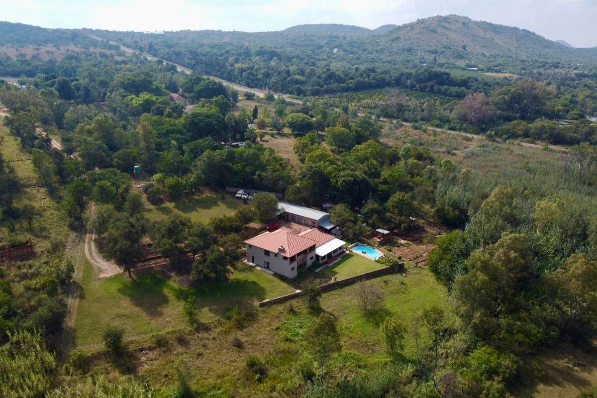 Aerial view of a farm property featuring a main residence, swimming pool, and surrounding landscaped grounds set within a scenic rural landscape.