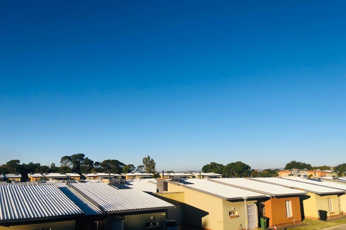 An elevated view overlooking a residential townhouse complex with uniform corrugated metal roofing and paved access paths.