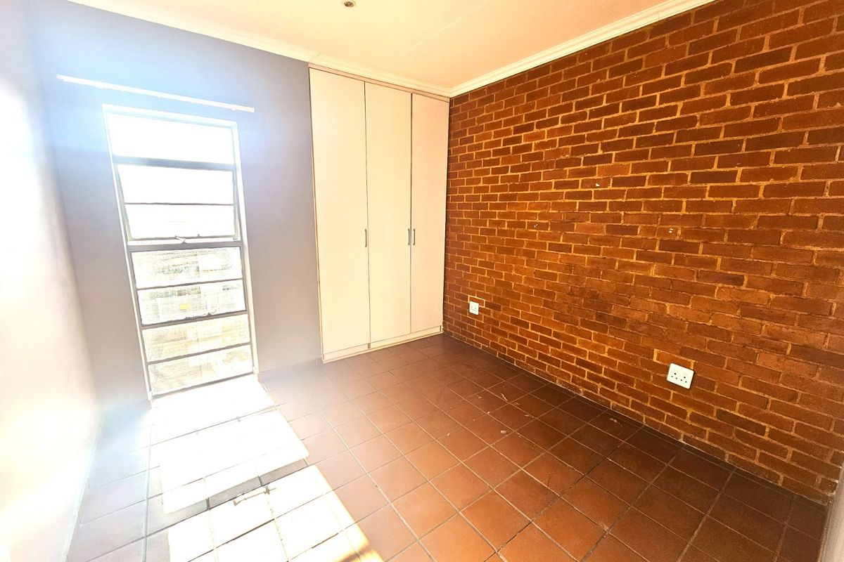A bedroom featuring a prominent exposed brick feature wall, tiled flooring, and built-in wardrobe storage.