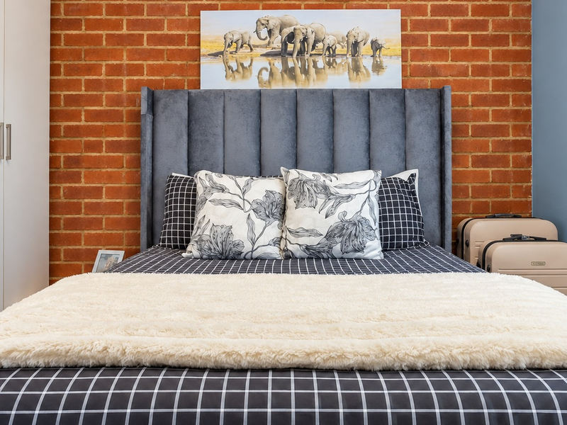 A well-maintained bedroom featuring a striking exposed brick feature wall and a functional built-in wardrobe.