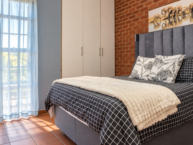 A well-lit bedroom featuring an exposed brick wall, built-in cupboards, and tiled flooring, offering a comfortable and functional living space.