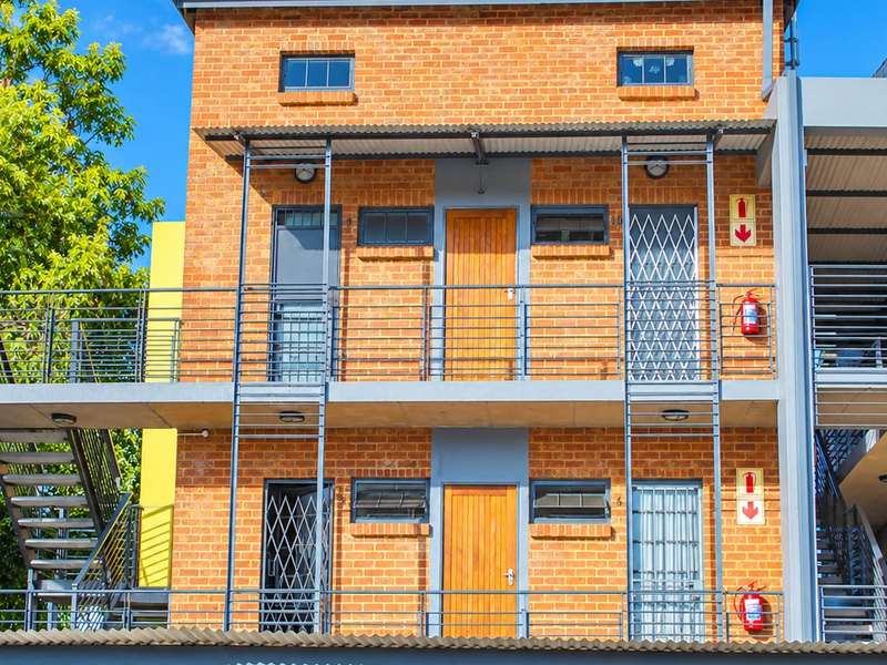 A multi-story apartment building facade featuring exposed brickwork, external metal staircases, security gates, and balcony access points.