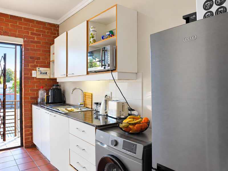 A functional kitchen featuring exposed brick walls, white cabinetry, tiled flooring, and direct access to an outdoor balcony area.