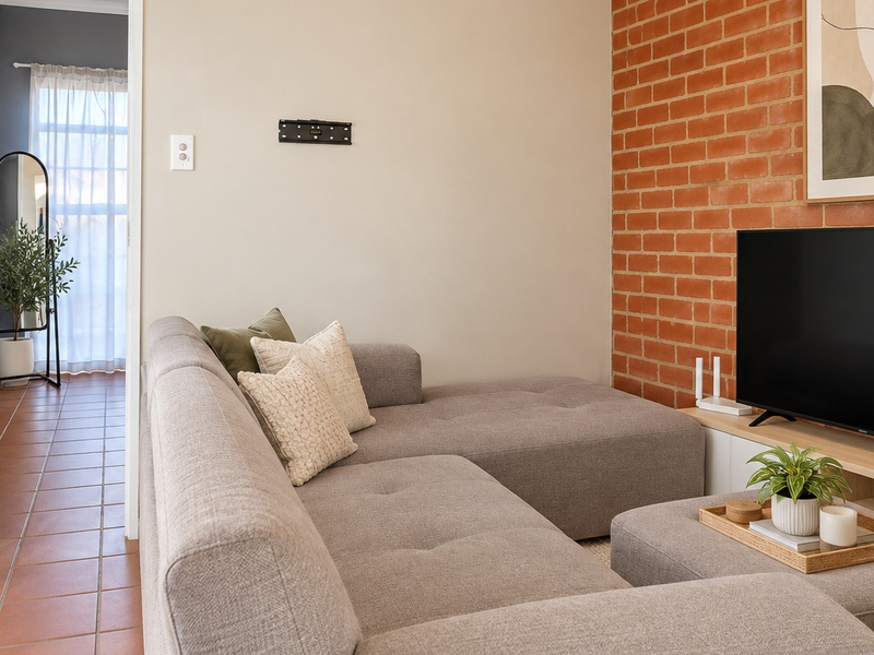 A cozy living room featuring an exposed brick accent wall, neutral tones, and tiled flooring, creating a warm and inviting atmosphere.