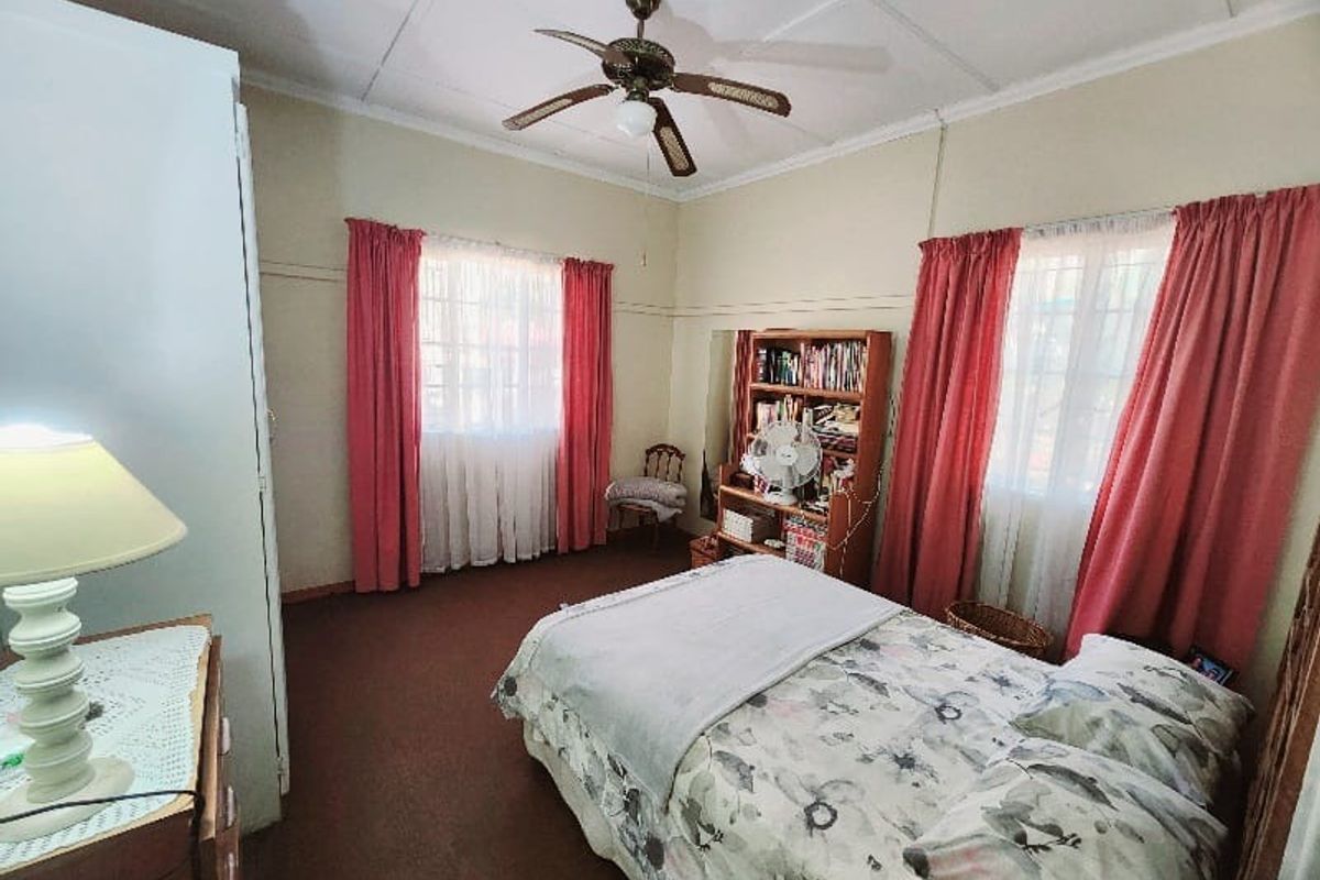 A spacious bedroom featuring high ceilings with a central fan, large windows with natural light, and carpeted flooring.