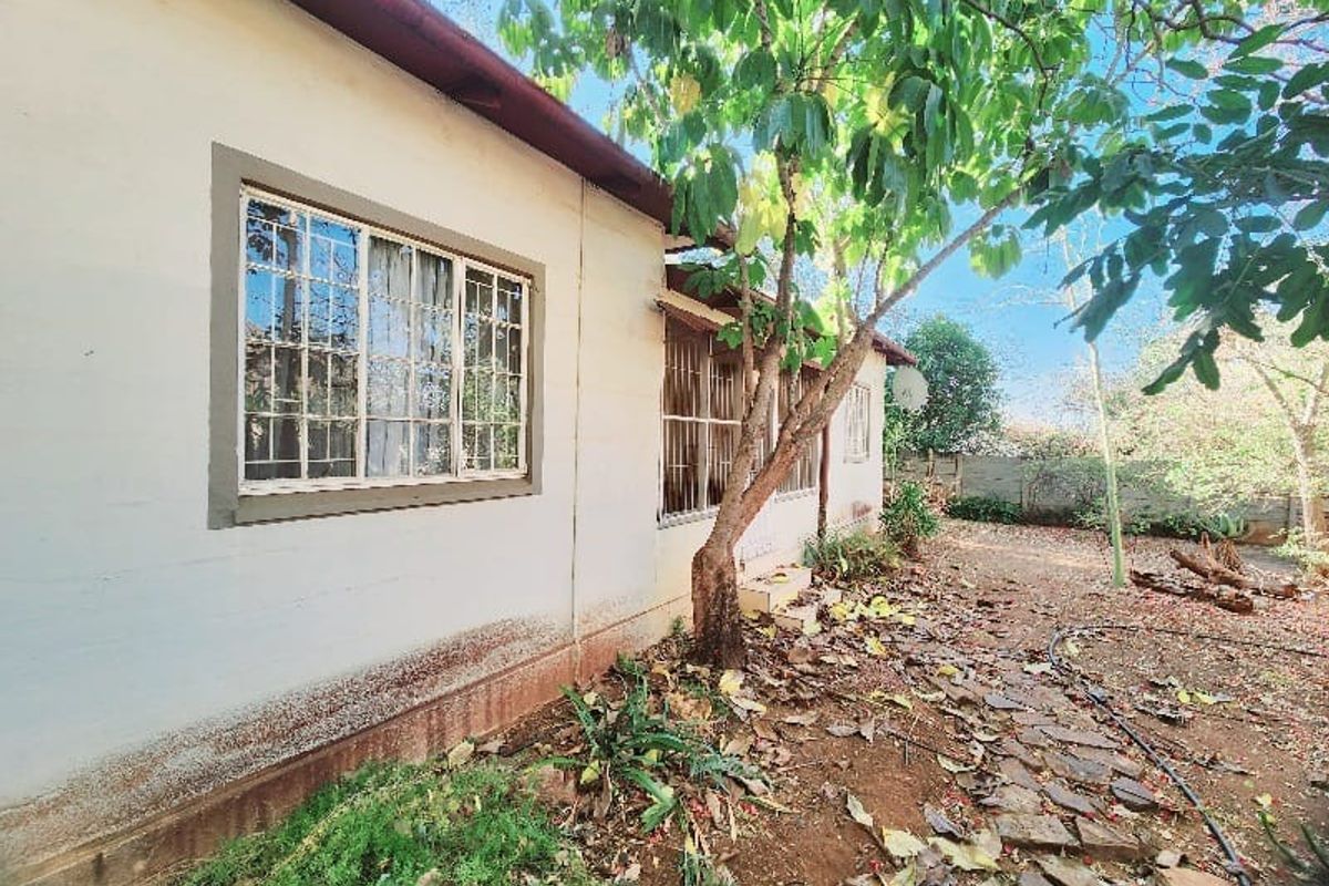 A view of the rear exterior facade of the house, featuring security-barred windows and a garden area with a stone pathway.