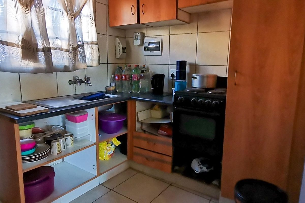 Compact kitchen featuring wooden cabinetry, tiled splashbacks, a built-in stove, and a single basin sink.