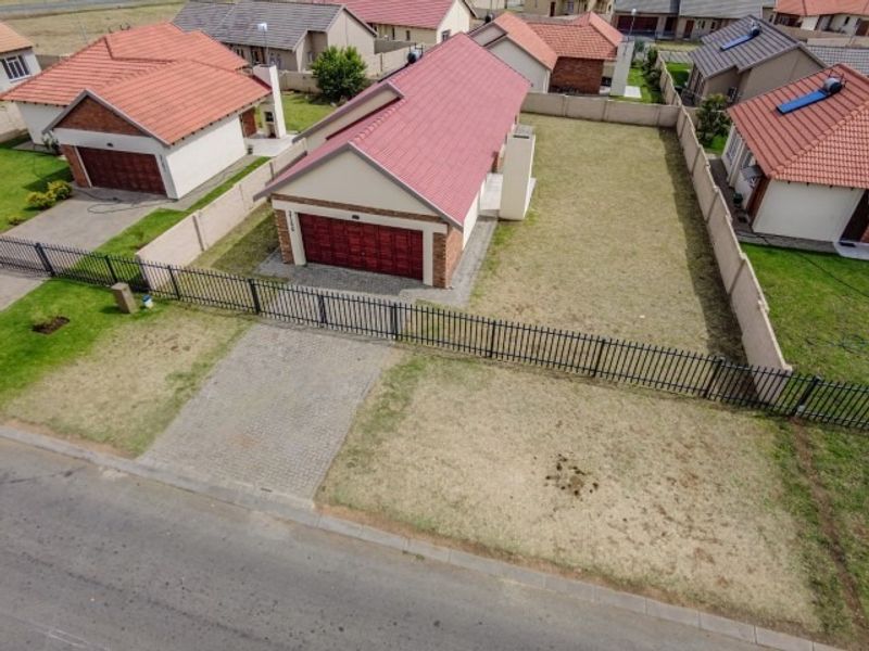 Aerial view of a residential property featuring a metal roof, double garage, paved driveway, and enclosed garden area within a suburban estate.