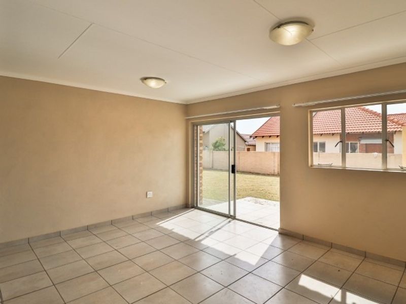 An empty, sunlit living room featuring neutral tiled flooring, flush mount lighting, and a sliding glass door providing direct access to the rear garden.