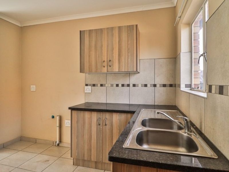 A functional kitchen area featuring laminate cabinetry, granite countertops, a double stainless steel sink, and tiled splashbacks in a clean, empty space.