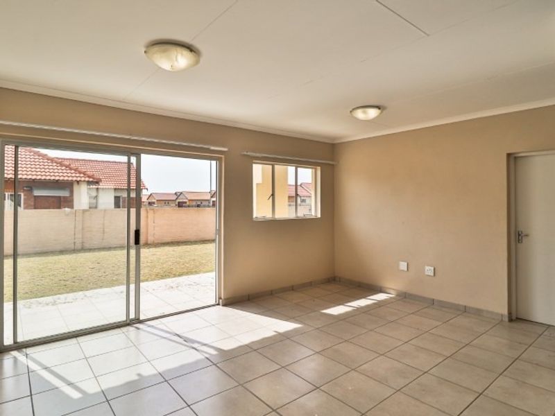 A bright, empty living room featuring tiled flooring, flush mount lighting, and a large sliding glass door providing access to the rear garden.
