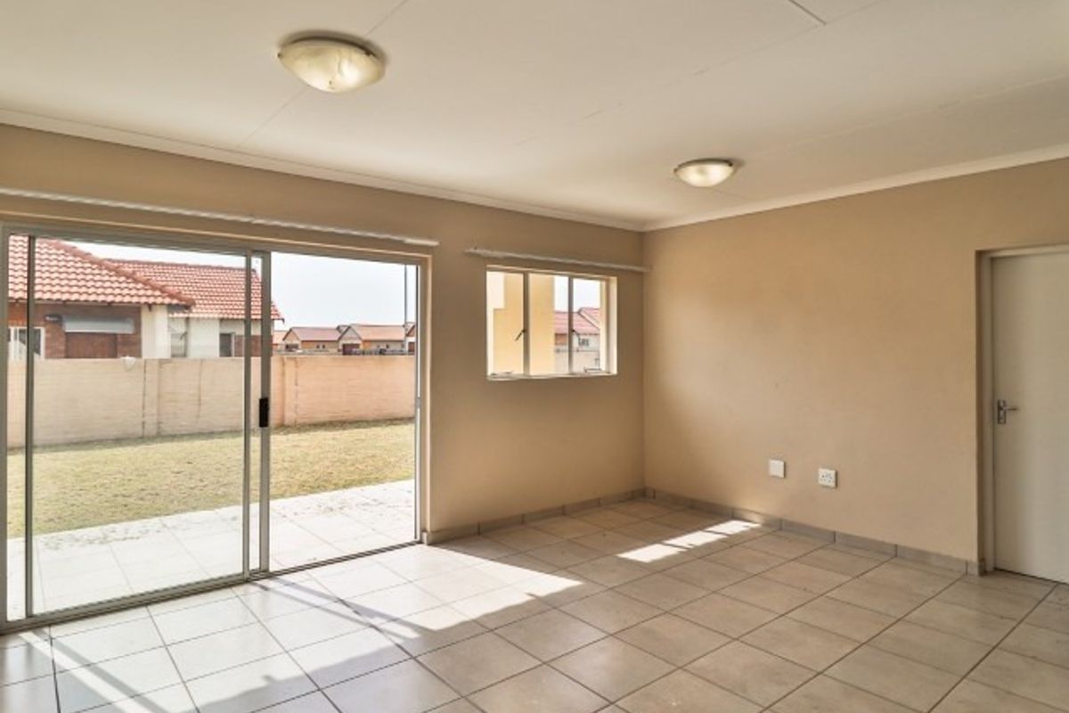 A bright, empty living room featuring tiled flooring, flush mount lighting, and a large sliding glass door providing access to the rear garden.