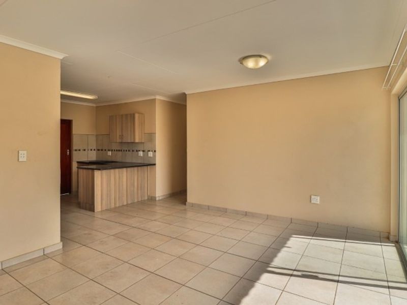 An open-plan living and kitchen area featuring neutral tiled flooring, built-in kitchen cabinetry, and a breakfast counter, offering a clean and versatile living space.