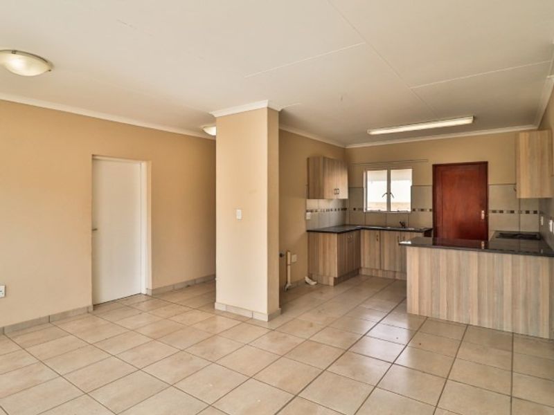 Spacious open-plan living and kitchen area featuring tiled flooring, neutral walls, and functional built-in cabinetry with a breakfast bar.