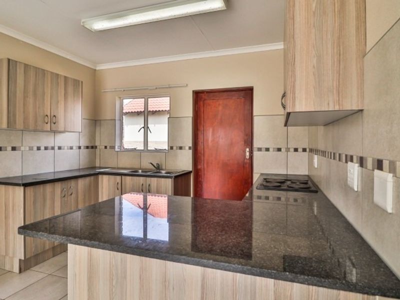 A functional kitchen featuring laminate cabinetry, granite countertops, a built-in electric hob, and tiled splashbacks, offering a clean and practical workspace.