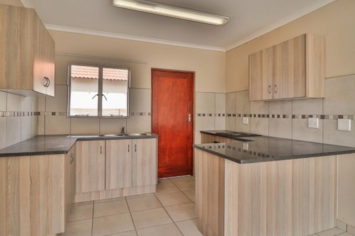 A functional kitchen featuring light wood-look cabinetry, dark countertops, tiled backsplash, and ceramic flooring, presented in a clean, empty state.