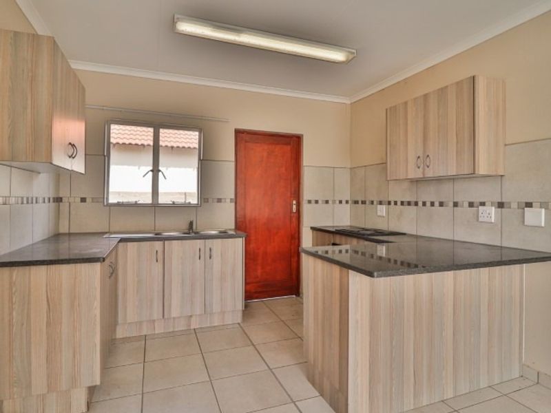 A functional kitchen featuring light wood-look cabinetry, dark countertops, tiled backsplash, and ceramic flooring, presented in a clean, empty state.