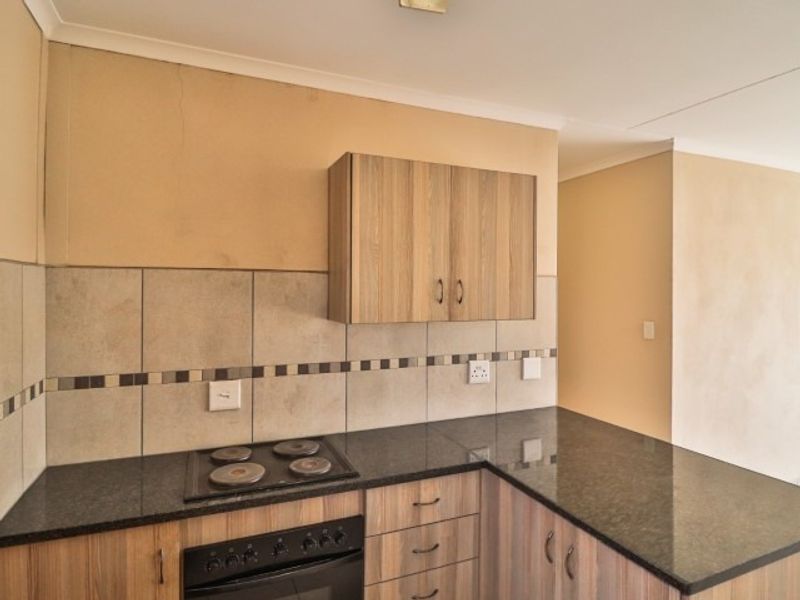A functional kitchen featuring wood-look cabinetry, dark granite countertops, a built-in electric hob and oven, and a tiled backsplash.