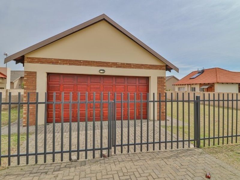A well-maintained detached double garage featuring a brick facade, paved driveway, and secure metal perimeter fencing.