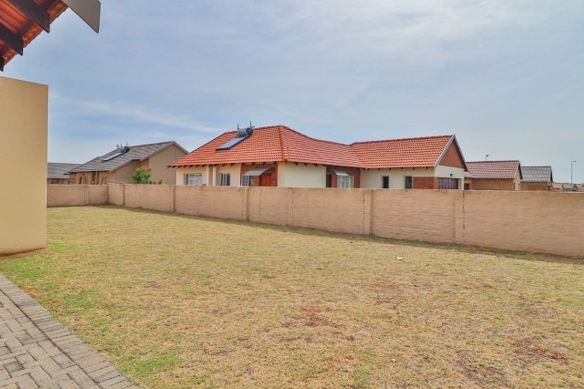 A spacious rear garden featuring a paved patio area, a large lawn, and a high perimeter wall, offering a private outdoor space.