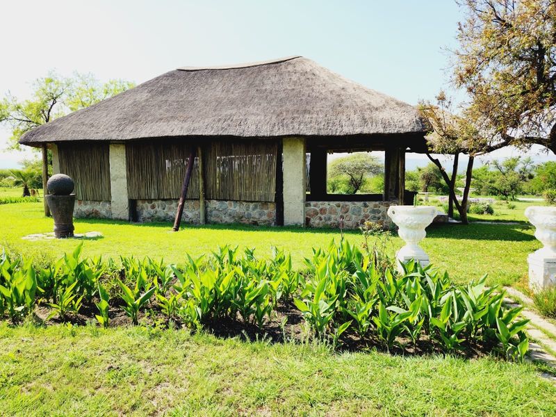 An open-air thatched lapa featuring stone masonry base and reed screening, set within a landscaped garden area.