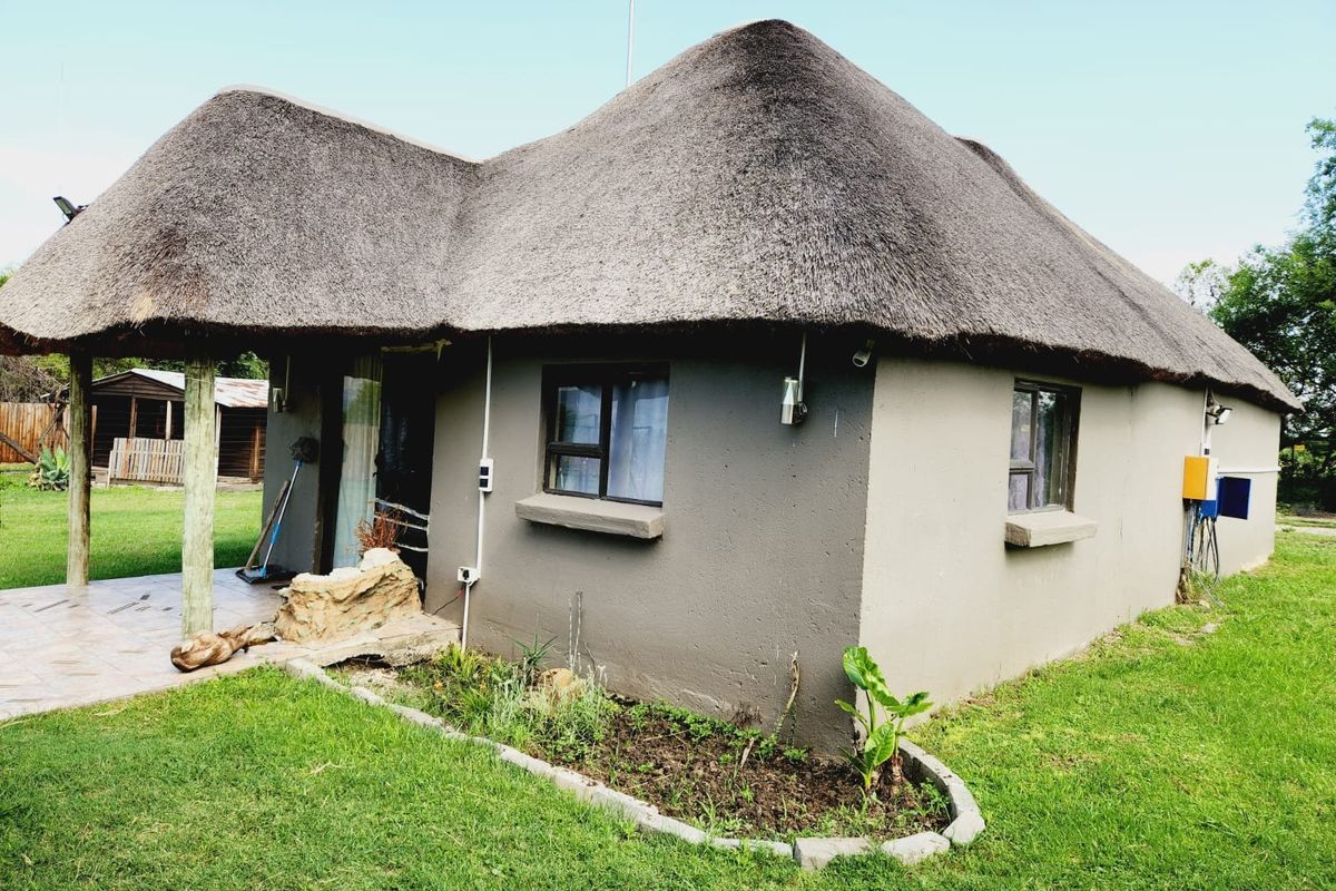A rustic farm-style cottage featuring a traditional thatch roof, a covered patio area, and established garden surroundings.
