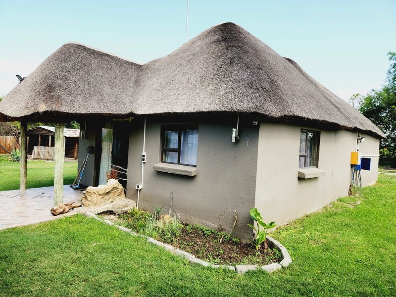 A rustic farm-style cottage featuring a traditional thatch roof, a covered patio area, and established garden surroundings.