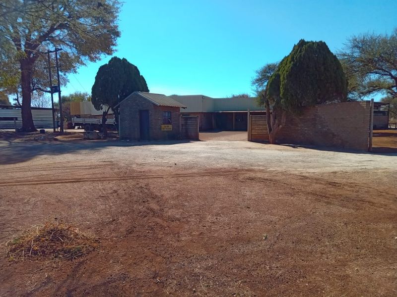 Front view of the farm property featuring a brick security gatehouse, perimeter walling, and an expansive unpaved driveway area.