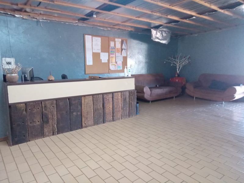 A rustic reception area featuring a timber-clad desk, tiled flooring, and an unfinished exposed ceiling structure.
