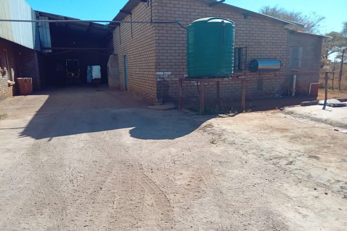 Rear exterior view of a farm building featuring brick construction, a metal roof, and an elevated water storage tank.