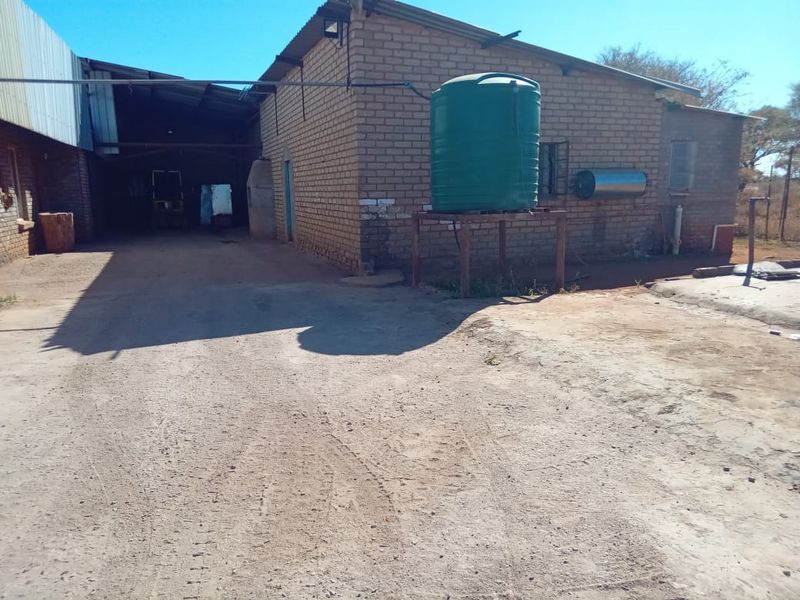 Rear exterior view of a farm building featuring brick construction, a metal roof, and an elevated water storage tank.