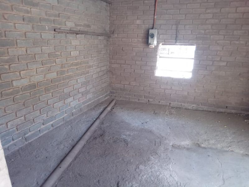 An unfinished utility space featuring exposed brick walls and a concrete floor, suitable for storage or workshop conversion.