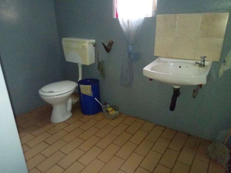 A functional bathroom featuring a wall-mounted basin with tiled splashback and a standard flush toilet, finished with ceramic tile flooring.