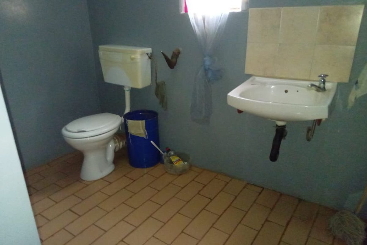 A functional bathroom featuring a wall-mounted basin with tiled splashback and a standard flush toilet, finished with ceramic tile flooring.