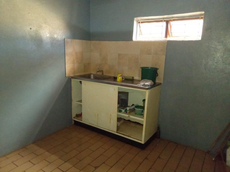 A basic kitchen area featuring a single stainless steel sink, tiled splashback, and built-in base cabinetry with tiled flooring.