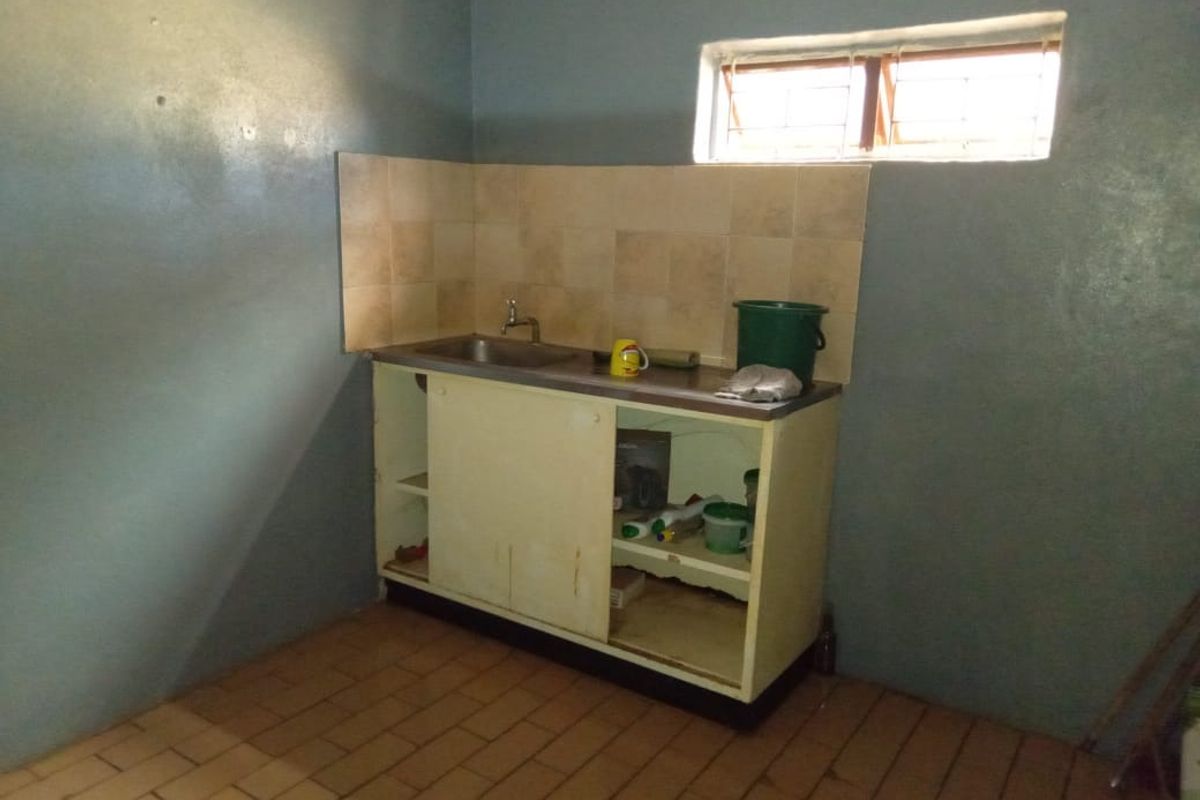 A basic kitchen area featuring a single stainless steel sink, tiled splashback, and built-in base cabinetry with tiled flooring.