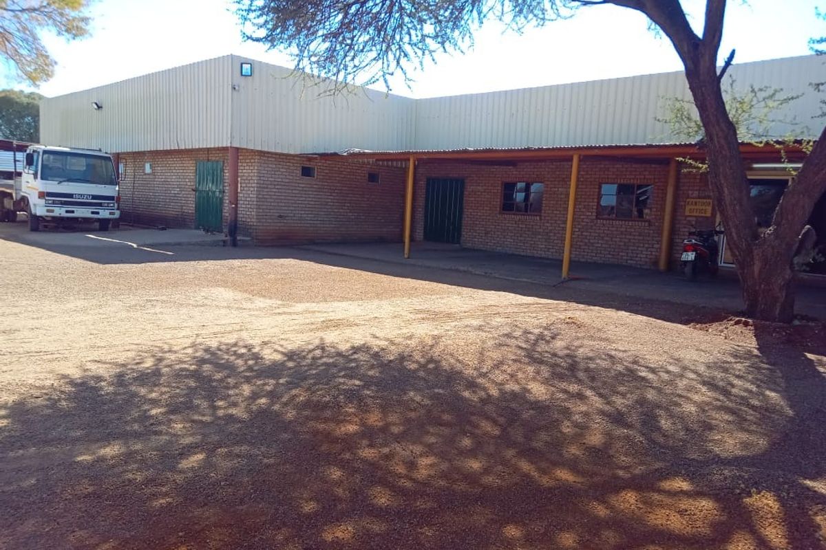 Front exterior view of a farm building featuring brick construction, corrugated metal roofing, and a covered walkway area.