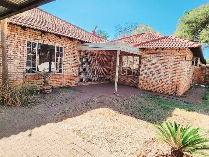 Rear view of a brick-built house featuring a paved patio area, covered veranda, and established garden space.