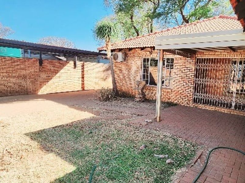 A rear exterior view featuring a brick-walled courtyard, a paved patio area, and a covered walkway, offering a private outdoor space.