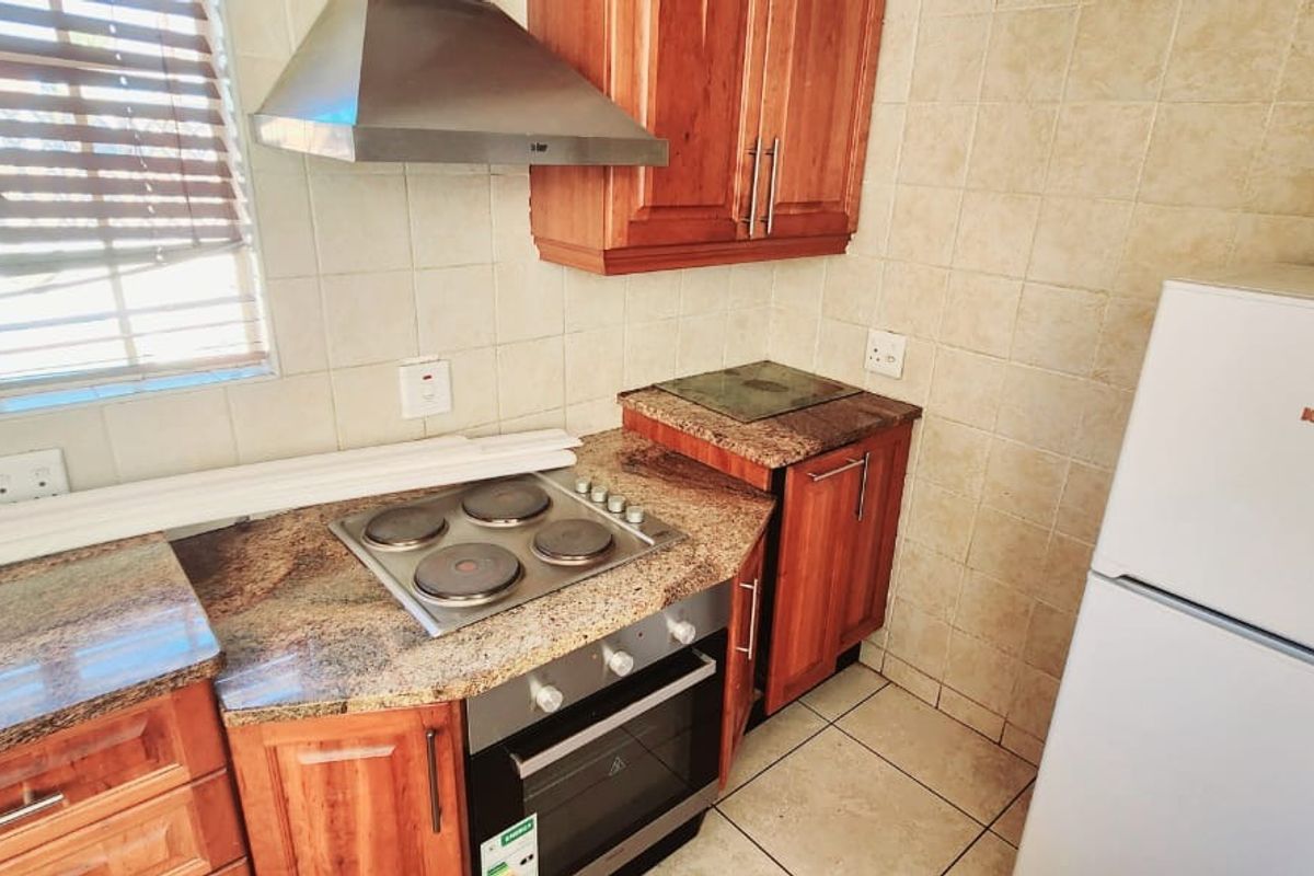 A functional kitchen featuring wooden cabinetry, granite countertops, a built-in oven with electric hob, and a stainless steel extractor fan.