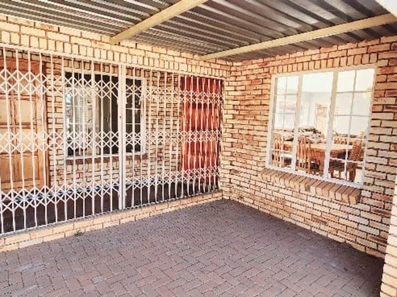 A covered patio area featuring face-brick walls, paved flooring, and a metal security gate over the entrance.