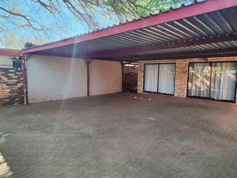 A spacious paved carport area with a metal roof structure, providing covered parking and direct access to the main building via sliding glass doors.