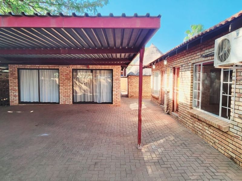A paved outdoor area featuring a covered carport structure, face-brick exterior walls, and an external air conditioning unit.